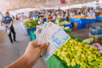 Turkish lira banknotes in hand against the background of vegetables at the farmer's market. The concept of consumer economy and inflation of the national currency of Turkey. - obrazy, fototapety, plakaty