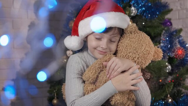 Happy child Christmas eve with teddy indoor. A happy little girl embrace the teddy toy by the Christmas tree. A concept of recieve New Year gift in the room.