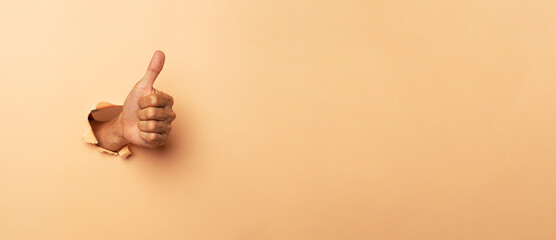 Close-up of male hand showing thumbs up on a brown background.. - obrazy, fototapety, plakaty