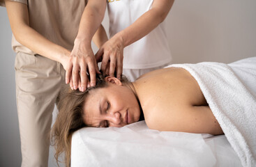 Fototapeta na wymiar Beautiful young woman lying with closed eyes and having head massage at spa in four hands. masseur student massage training. beauty, lifestyle and relaxation