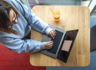 A young woman in glasses works behind a laptop at the workplace.