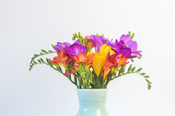 Cropped closeup of bright freesia flowers in green vase against white background (selective focus)