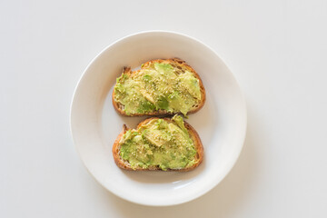 High angle closeup of toasted sourdough bread with avocado and hemp seeds on white plate