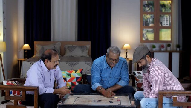 Three old men playing carrom together in their old age home - carrom board  an indoor game. Old friends spending quality time together at home - leisure time  togetherness and bonding  friendship 