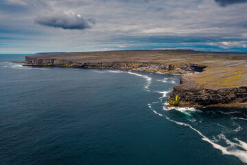 View on rough stone coast line of Aran island, county Galway, Ireland. High stone cliff. Blue cloudy sky and ocean surface. Aerial view. Stunning Irish nature landscape.