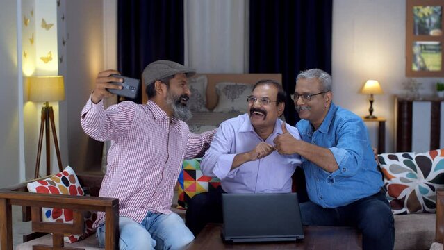 Three gentlemen in casual clothes clicking a selfie on their smartphone - leisure time  old age. Three cheerful old Indian friends doing a thumbs-up gesture while clicking pictures - a modern lifes...