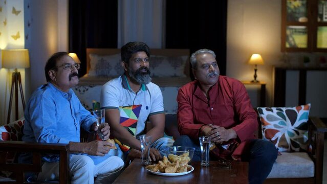 Three middle-aged old friends eating snacks while watching television - fun and entertainment  refreshment and snacks  party time. Friends in their late 40's in a hotel room watching TV 