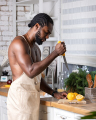 Black man cooking breakfast or lunch on kitchen at home. African American man wearing an apron preparing lemon.