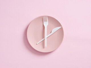 Knife and fork on pink plate designed as clock. Intermittent fasting, lunchtime, weight loss, meal plan or diet