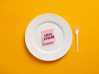 Notepaper with the word less sugar on a white plate. Less sugar intake and healthy nutrition