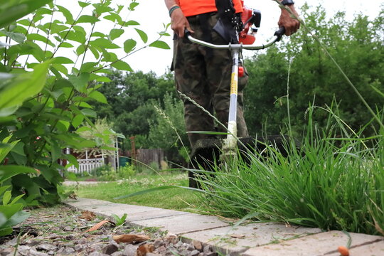 A gardener mows the grass with a brush cutter.