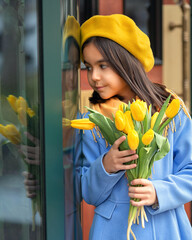 Portrait of a happy girl with a bouquet of yellow tulips on a walk in spring. Flowers for International Women's Day.