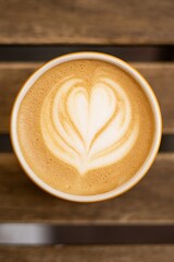Cup of cappuccino latte art heart shape foam. Top view of coffee on a wooden table in a street cafe