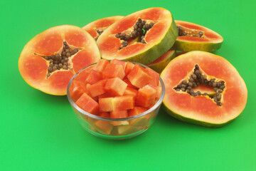 Sliced red papaya fruits in glass bowl and on green background close up.	