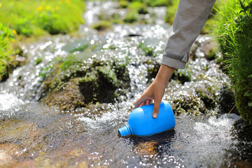 Hiker hand filling canteen with river water