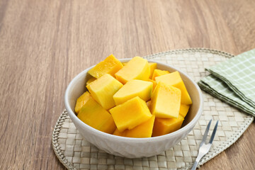 A bowl of sliced ​​fresh mango cubes on wooden background. Copy space
