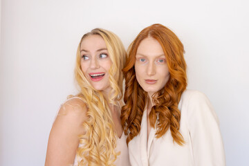 Beauty picture gorgeous happy optimistic beautiful blonde and redhead women posing isolated over light wall background talking gossip to each other.