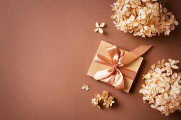 Gift box with golden ribbon and dry grass and flowers on brown background
