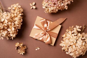 Gift box with golden ribbon and dry grass and flowers on brown background