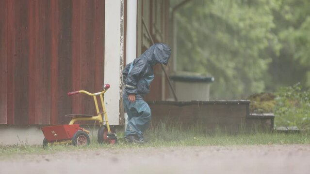 SLOW MOTION - A cute child plays with a downpipe in heavy rainfall
