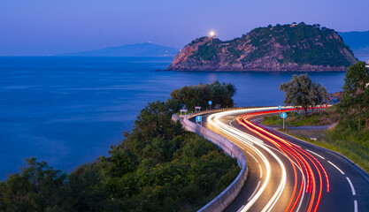 Car lights on the road on the coast of Euskadi. Getaria lighthouse at dusk. © poliki
