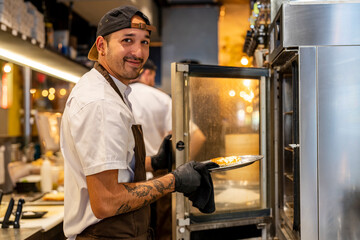 Smiling chef holding food in plate standing by oven at restaurant