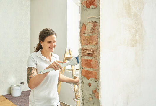Smiling painter doing final paint with brush in apartment