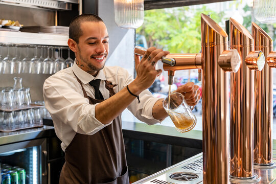 Bartender filling beer in glass from tap at bar