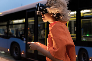 Woman enjoying wearing virtual reality headset by bus at night