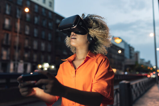 Woman holding controller wearing virtual reality headset at night