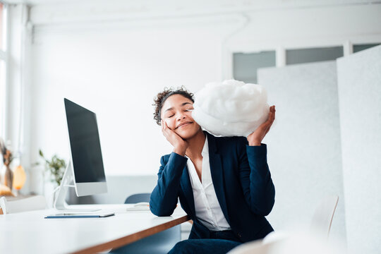 Smiling businesswoman with eyes closed holding cloud in office