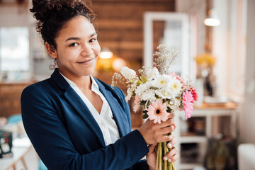 Smiling young businesswoman with flowers in office