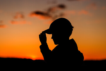 Silhouette of boy with cap at sunset