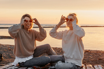 Smiling daughter and mother covering eyes with strawberries at beach on sunset