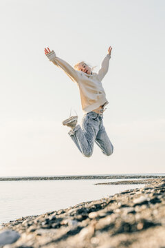 Teenage Girl With Arms Raised Jumping At Beach