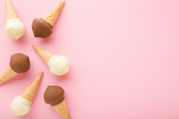 Waffle cones of white vanilla and black chocolate ice cream on light pink table background. Pastel color. Closeup. Cold sweet snack in summer. Empty place for text. Top down view.