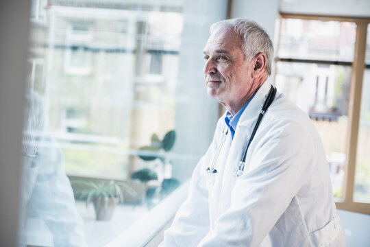 Smiling doctor looking through window at hospital