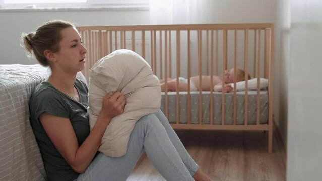 Depressed mother screaming with anger and desperation in pillow to overcome negative emotions, suffering postnatal depression because of lack of help and support with childcare routine