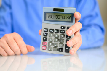 Mann am Schreibtisch mit einem Taschenrechner in der Hand auf dem Grundsteuer steht