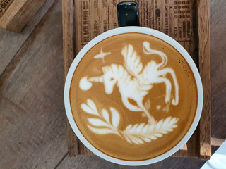 coffee cup with latte art unicorn painting on wooden table