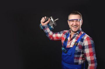 Portrait of an attractive repairman in uniform and plaid shirt with stubble on his face, demonstrating equipment in his hand, studio shot