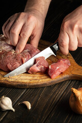 The chef cuts raw beef meat on a cutting board before baking. Peasant foods