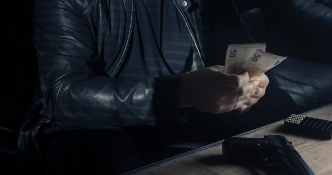 a mobster or drug dealer is counting money and has a gun on the table