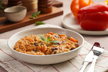 Grain dish - Millet with tomatoes, beans, carrots and spices, mint in a white bowl on a concrete round tray with checkered linen kitchen towel on purple background