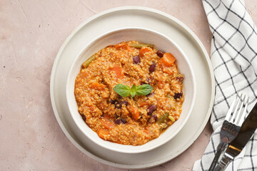 Grain dish - Millet with tomatoes, beans, carrots and spices, mint in a white bowl on a concrete round tray with white checkered kitchen towel on purple background, top view, space for text