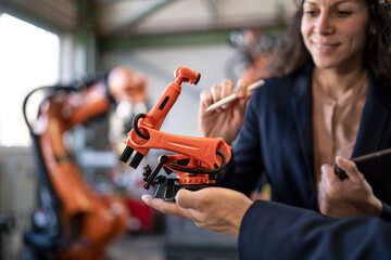 Close-up of man engineer holding model of industrial robotic arm and showing to collegue in factory.