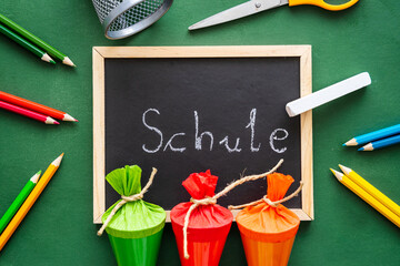 Draufsicht auf eine Tafel mit dem deutschen Wort Schule, drei kleine Schultüten und Farbstifte auf...