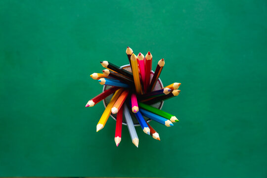 Draufsicht auf Farbstifte in einem Gef&auml;&szlig; auf einem gr&uuml;nen Tisch. Bildung.