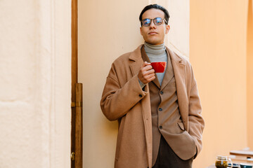 Young man wearing glasses drinking coffee while standing on city