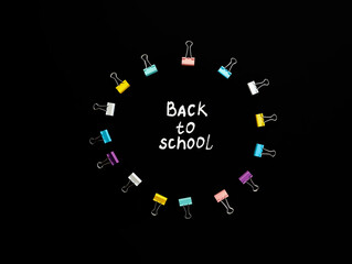 circle of multi-colored paper clips with white handmade inscription back to school in middle, on black background